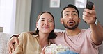 Happy couple, tv remote and popcorn while watching a funny comedy movie while enjoying online streaming service and a laugh in the living room at home. Asian man and woman enjoying fun entertainment