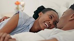 Happy black couple embrace and bonding in bed, touching, flirting and loving. Smiling African American husband and wife being romantic, enjoying their time together indoors, bedroom fun affection