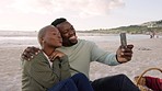 Happy couple taking a selfie with a phone while on a beach picnic date during spring. Black man and woman taking picture with a smartphone camera and making silly faces while relaxing in nature.