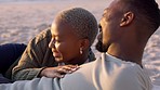 Couple, beach and sunset with a smile, love and hug together while relax on the sand together in summer. African american man and woman enjoy romantic holiday, vacation or date at the ocean at dusk