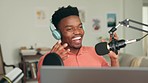 African radio presenter talking with a microphone in his home studio with headphones and a laptop. Happy black man recording a podcast with technology equipment in his creative office at his house.