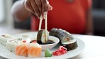 Woman eating sushi, food or health meal with soy sauce in restaurant, home kitchen table or house room desk for lunch. Zoom on black hands and chopsticks to eat japanese fish, salmon or rice in leaf 