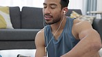 Man on a phone with earphones listening to music and typing a message before a fitness workout. Guy with a wellness, health and active lifestyle sitting on the floor getting ready to exercise at home