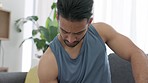Health, training and exercise with bodybuilder lifting weights and being active while sitting on sofa at home. Athletic male focused on fitness, cardio and strength endurance practice in living room