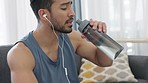 Tired, exhausted and thirsty man drinking water and wearing earphones to listen to music after a fitness workout at home. Male doing exercise for wellness, health and an active lifestyle while resting
