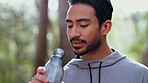 Health, fitness and man drinking water in a park resting, thirsty and tired from training, workout and exercise. Dehydration, nature and young athlete with a bottle of a healthy liquid for energy
