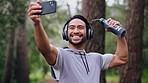 Fitness man, selfie and headphones during forest workout listening to music and taking pictures for social media of influencer content. Happy asian male out for a run, training and exercise in nature
