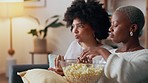 Friends on sofa with popcorn, watch movie or television series together in living room. Black woman with friend relax, eating corn snack while watching film or tv on couch in home lounge