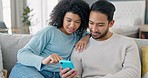 Happy multiracial couple on couch in living room chatting, scrolling social media apps and streaming a movie. Black woman and asian man on sofa online using smartphone for internet and planning date.