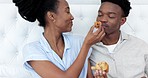 Love, food and couple eating a cupcake in the bedroom in the morning for a romantic breakfast together. Smile, happy and young black woman sharing sweets or muffins with her young partner at home