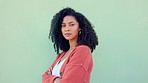 Black woman, confident beauty and young model pose for portrait with afro hair on green background. African girl in orange sweater, fold arms with cool serious face and casual fashion lifestyle