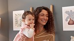Young mother holding happy baby in arms, smiling and playing together. Portrait of mom embracing baby girl, singing and laughing with her in their home. Family, love and care of infant child