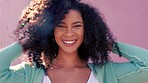 Portrait of a woman touching and moving her afro standing outdoor by a pink background. Happy, smile and beautiful latin girl embracing and playing with her natural curly hair while outside in sun.