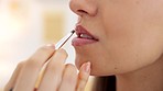 Painting young woman with pink lipstick on her mouth with brush, makes a kissing movement with lips and with a smile of excitement. Beauty products, cosmetics and makeup are part of female self care 