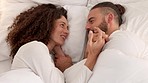 Couple in bed together talking, funny conversation and holding hands before sleep for love, care and intimacy. Happy marriage millennial husband, wife or people relax in bedroom, hotel or home above