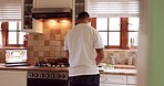 Man cooking food in kitchen in his home, cutting vegetables and using a laptop for recipe. Young guy alone, using his computer to follow recipes for dinner or supper. Chef, cook and a healthy meal