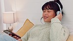 Phone, music and relax with a woman streaming audio on headphones while lying in bed in the bedroom of her home. Freedom, wellness and mental health with a young female relaxing with a radio playlist