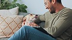 Young man with dog pet on sofa in his living room apartment for support, love and care. Happy guy relax on couch and smoke, kiss and play with his loyal puppy, animal or jack Russell terrier