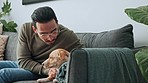 Happy, relax and man bonding with dog on a sofa, playing and showing affection for his puppy in a living room. Cheerful, loving and asian male enjoying time with his pet on a couch, playful together