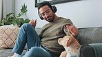 Man, phone and headphones on sofa with dog listening to music, podcast or online social media. Living room, relax and happy owner bonding with pet on couch, audio or radio streaming on mobile at home