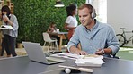 Advertising worker writing in notebook with laptop and headphone in a creative marketing office. Businessman listening to music or podcast while working on report or proposal on paper in startup job