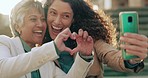 Heart, hand sign and friends take a selfie for memories and love laughing at funny jokes outdoors together. Smile, memory and mature women enjoy a happy holiday vacation sharing it on social media