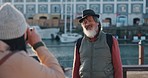 Man, elderly and photo as tourist pose on dock by sea, building and boat on vacation, holiday or travel. Smile, asian and senior in retirement with photographer for portrait by water in Cape Town