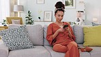 Phone, social media and contact with a woman typing while sitting on her sofa to relax alone in her home. Living room, internet and mobile with a young female laughing while reading a text or meme