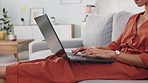 Laptop, freelancer and woman typing on a keyboard while sitting on sofa in the living room. Computer, technology and girl working on a freelance project while relaxing on the couch in her modern home