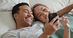 Phone, social media and communication with a couple in bed to relax, laughing and relaxing in the bedroom of the home together. Diversity, internet and mobile with a man and woman happy in the house