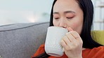 Woman, coffee and relax on sofa with phone, social media or text message in home. Living room, tea and Japanese female on 5g smartphone internet surfing, web browsing or networking online on apps.