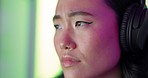 Face, focus and gaming with a woman in headphones playing a video game against a neon background. Thinking, esports and internet with a young female gamer live streaming on a streaming service