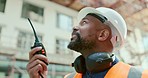 Construction site, black man and building manager with walkie talkie for logistics, development and update. Project management, communication and construction employee speaking with portable radio.