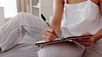Woman writing in journal, hand notes in bedroom with pen and student learning education at home. Creative writer with notebook, planning schedule in morning routine and sitting on bed with diary page