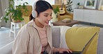 Happy, smile and woman on laptop, headphones and listening to music, social media and movie subscription in home. Content asian female typing, watching and streaming series on weekend while relax