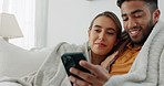 Sofa, interracial and couple phone social media with happy cuddle in cozy winter blanket at home. Soulmate, relax and love of indian male and caucasian woman enjoying funny social network talk. 

