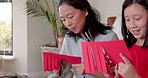 Family, children and creative with an asian woman and daughter cutting red paper together in the living room of their home. Kids, love and design with a mother and girl child bonding over creativity