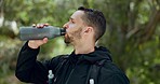 Hiking, nature and man drinking water in bottle while on outdoor adventure trail hike in forest. Travel, freedom and healthy young guy enjoying refreshing drink for hydration while trekking in woods.