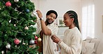 Christmas, tree decorating and young black couple celebrate in living room, family home and house for happy celebration event. Man, woman and winter holiday time, festive lights and bauble decoration