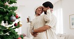 Christmas, hug and couple with coffee, tree and love in the living room of a house together. Happy, smile and African man and woman with tea to relax while dancing during a festive celebration