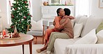 Couple, love and christmas celebration in a living room with black woman kiss, hug and relax with man on a sofa. Black family, christmas tree and woman embracing guy on a couch, enjoy festive holiday