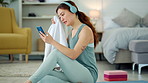 Woman, phone and yoga with rest, towel and music while sitting, floor and relax in living room. Girl, headphone and smartphone for streaming, video or reading while taking break, training or fitness