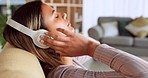 Woman, headphones and relax listening to music on living room sofa with eyes closed at home. Female enjoying calm audio track with wireless headset relaxing in comfort on couch at the house indoors