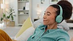 Relax, music and black woman with headphones on sofa for wellness rest and streaming with satisfied smile. Self care, happy and comfortable girl listening to musical audio app in home bedroom.