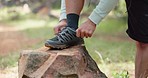 Sports shoes, hiking and man tie lace on rock outdoors in nature park. Fitness hike, mountain climbing and young male athlete healthy wellness training in forest or exercise sport trekking footwear