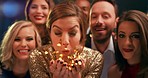 Woman blowing sparkly confetti celebrating at a party with a group of friends