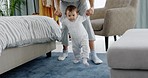 Baby learning and walking with support of mother for first steps, healthy body development and growth in living room. Mom holding hands for teaching young toddler kid balance, care and walk in lounge