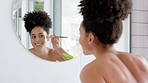 Bathroom, mirror and makeup with a black woman applying blusher to her face or cheek in the morning at home. Skincare, beauty and cosmetics with an attractive young female getting ready in her house