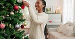 Christmas, black woman and decoration for tree, holiday or happy with celebration, smile or relax. Young female,  festive girl or content being creative, prepare for Xmas in living room for happiness