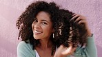 Beauty, hair and natural kinky afro with black woman styling her curls, proud and happy against a purple wall in an urban city. Portrait of a positive African American feeling proud after haircare